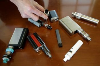A variety of vape devices are spread out on a table. Learn more about tobacco prevention and cessation in Colorado.