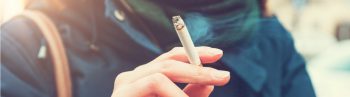 A woman in a blue coat and scarf is smoking a cigarette. Learn more about quitting tobacco.